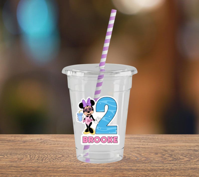 May include: A clear plastic tumbler with a lid and a purple and white striped straw. The cup features a graphic of a cartoon mouse wearing a pink bow and heart-shaped sunglasses, a large blue number two, and the name BROOKE in pink letters.