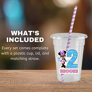 May include: A clear plastic cup with a lid and a purple and white striped straw. The cup features a graphic of a cartoon mouse wearing sunglasses and a pink outfit, a large blue number 2, and the name BROOKE printed in pink capital letters.