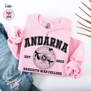May include: Light pink sweatshirt with the word "ANDARNA" in black block letters. Below the word is a circular graphic with the text "FLY OR DIE" and "BASGIATH WAR COLLEGE". The sweatshirt also has the text "EST. 2023".