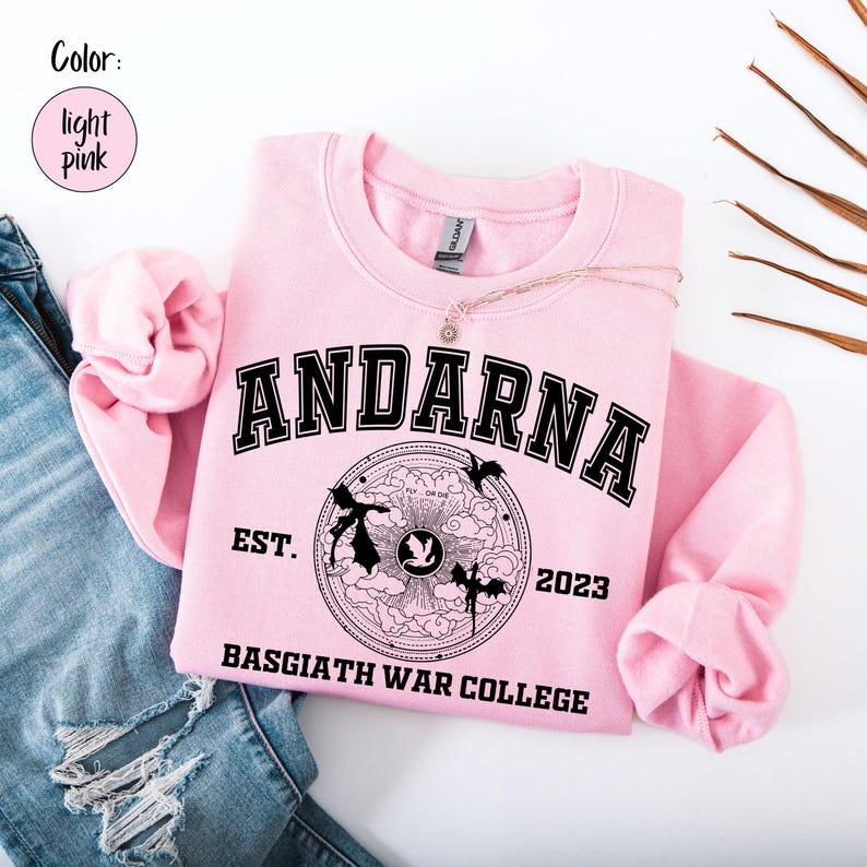May include: Light pink sweatshirt with the word "ANDARNA" in black block letters. Below the word is a circular graphic with the text "FLY OR DIE" and "BASGIATH WAR COLLEGE". The sweatshirt also has the text "EST. 2023".