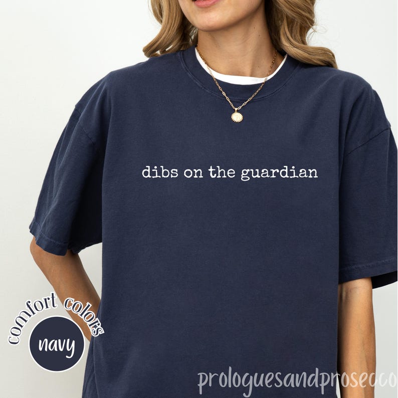 May include: A navy blue short-sleeved t-shirt featuring the white text "dibs on the guardian" printed across the chest. The shirt has a crew neckline and a relaxed fit. A small circular graphic in the corner displays the text "comfort colors navy".