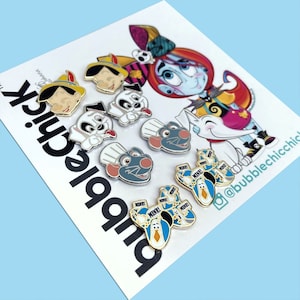 Può includere: Una collezione di spille smaltate raffiguranti personaggi dei cartoni animati. Le spille includono immagini di Pinocchio, un cucciolo dalmata, uno chef ratto e pinguini con la scritta "MINE!". Le spille sono su una carta bianca con la scritta "bubble chick".