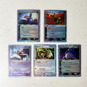 Puede incluir: Cinco cartas coleccionables de Pokémon con personajes como Hitmonchan ex y Umbreon ex. Cada carta tiene un diseño holográfico e incluye arte de personajes, HP y detalles de ataque. Las cartas también incluyen Deoxys ex, Rayquaza ex y Snorlax ex.