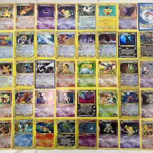 May include: A collection of vintage Pokémon trading cards, featuring various characters and designs. The cards have yellow borders and are arranged on a white surface. The image includes a variety of Pokémon, such as Charizard, Pikachu, and Mewtwo.