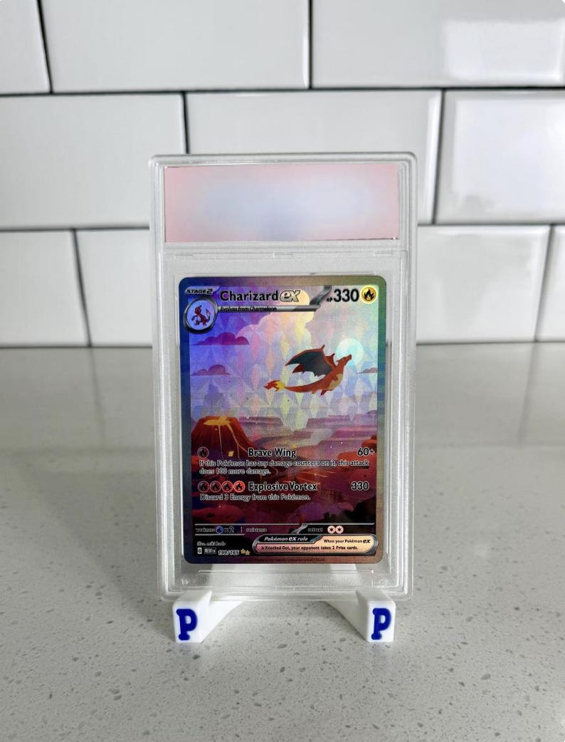May include: A Charizard EX Pok&eacute;mon trading card, graded and encased in a clear plastic holder. The card features a holographic image of a fiery dragon over a volcanic landscape. The card is displayed on a white stand.