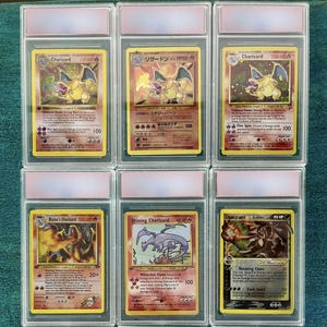 Könnte beinhalten: Sechs bewertete Charizard-Pokémon-Karten in Schutzhüllen. Die Karten zeigen verschiedene Charizard-Illustrationen, einschließlich japanischer Versionen. Die Karten befinden sich in transparenten Kunststoffhüllen mit rosa Etiketten.