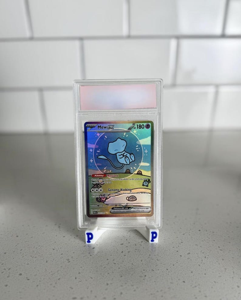 Op de afbeelding: Een beoordeelde Mew ex Pok&eacute;mon-verzamelkaart in een doorzichtige beschermhoes. De kaart heeft een holografisch ontwerp met een blauw Mew-personage. De kaart wordt weergegeven op een witte standaard met blauwe "P"-logo's.