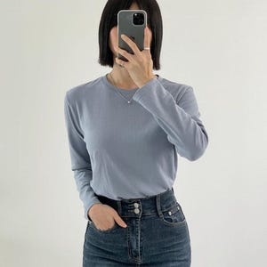 May include: A light blue long-sleeve shirt and dark wash denim jeans. The shirt has a crew neck and is paired with high-waisted jeans with a button closure. The outfit is simple and casual, suitable for everyday wear.