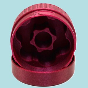 May include: A deep magenta-colored, plastic grinder with a ridged top and a star-shaped interior. The grinder is in two parts, with the top section slightly separated from the base, set against a light blue background.