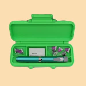 Op de afbeelding: Een groene plastic koffer, open om een ​​turkooizen medische pen, alcoholdoekjes en verschillende paarse naalden met dop te laten zien. De koffer is rechthoekig met een scharnierend deksel en compartimenten.