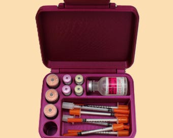 May include: An open, magenta-colored medical travel case containing vials, syringes, and a bottle with a red label. The case is organized with compartments for each item, suggesting a kit for medical supplies or medication.