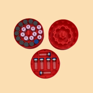 May include: Three red circular containers with various contents. One container holds multiple vials with pink and gray caps, another holds vials with clear liquid, and the third is empty. The containers are on a light orange background.