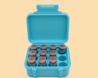 May include: A teal blue carrying case, open to reveal twelve small glass vials with brown lids. The case has a handle and a secure latch. The vials are arranged in a grid within the case.