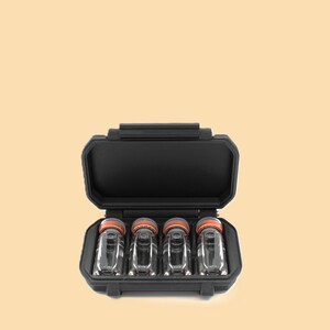 May include: A black, rectangular case with a hinged lid, open to reveal four small, clear glass vials with orange caps. The vials are arranged neatly inside the case, which is set against a light orange background.