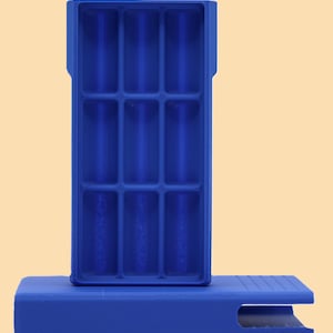 May include: A cobalt blue ice cube tray with a rectangular shape and nine individual compartments. The tray is resting on a matching blue base with a slot cut out of the side. The design is simple and modern.