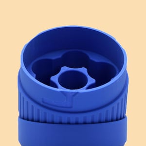May include: A close-up of a blue plastic bottle cap. The cap has a ridged base and a star-shaped design in the center. The cap is a vibrant blue color and is set against a light orange background.