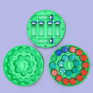 May include: A green plastic organiser with three circular sections. One section holds vials with blue and clear caps. Another section contains colourful caps in blue, green, and red. The third section is empty.