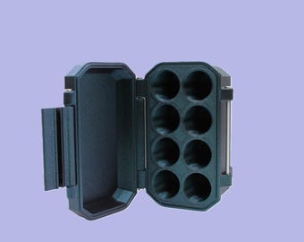 May include: An open, dark teal case with eight circular compartments. The case has a hinged lid and a latch on the side. The interior is a darker shade of teal than the exterior.