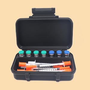 May include: Open black case containing medical supplies. The case holds several vials with green and blue caps, along with multiple syringes with orange caps. The case is open, revealing the contents.