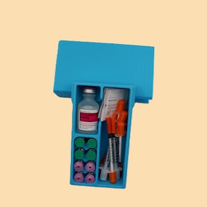 May include: A blue plastic medical kit with a hinged lid. Inside are vials, syringes, alcohol prep pads, and small containers. The vials are labeled "Bacteriostatic Water". The kit is on a light tan background.