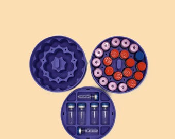May include: Three-part, deep purple, circular organizer. One section is empty with a floral design. Another holds vials with red and pink caps. The third section contains clear vials with blue caps.