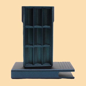 May include: A teal-colored, rectangular organizer with multiple compartments, standing on a matching base. The organizer has a grid-like interior, and the base features a grooved design. The overall aesthetic is modern and minimalist.