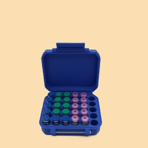 May include: A blue carrying case, open to reveal rows of small glass vials with blue, green, and pink caps. The case has a handle and a secure latch. The vials are arranged neatly inside the case.