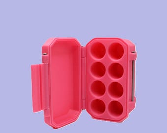 Puede incluir: Estuche rosa brillante de carcasa dura, abierto para revelar ocho compartimentos circulares. El estuche rectangular tiene esquinas redondeadas y una tapa con bisagras. La tapa está abierta, mostrando el interior. Cuenta con un cierre lateral y una bisagra gris.