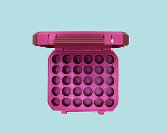 May include: A magenta plastic storage case, open to reveal a grid of circular compartments. The case has a handle and is set against a light blue background, designed for small items.