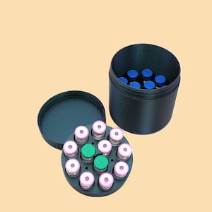 May include: A black container with a lid, holding several small glass vials. The vials have pink and green tops, and are arranged in a circular pattern. The container is open, revealing the contents.