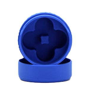 May include: A blue, two-piece grinder with a four-leaf clover-shaped interior. The top piece has a textured edge. The bottom piece is a simple cylinder. The grinder is made of plastic.