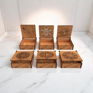 Peut inclure: Six boîtes en bois avec des couvercles à charnière, chacune avec un motif décoratif découpé au laser. Les boîtes sont ouvertes, révélant leurs intérieurs vides. Les couvercles sont ornés de motifs complexes, et les boîtes sont en bois clair.