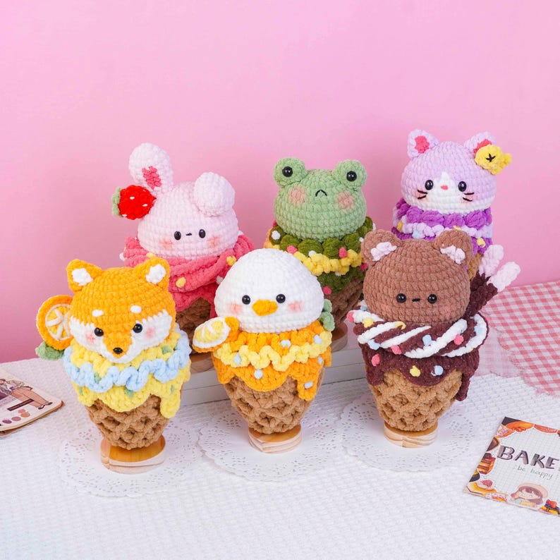 May include: Six crocheted plush toys shaped like ice cream cones, each featuring a different animal head including a fox, rabbit, frog, cat, bear, and bird. Each toy has a textured tan cone base and colorful yarn details representing toppings.