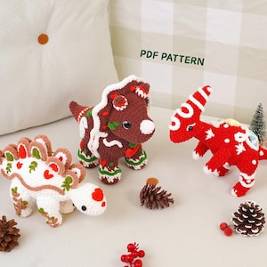 May include: Three crocheted dinosaur toys decorated like gingerbread cookies. One is white with red and green accents, one is brown with white icing details, and one is red with white stripes. The text PDF PATTERN is visible.