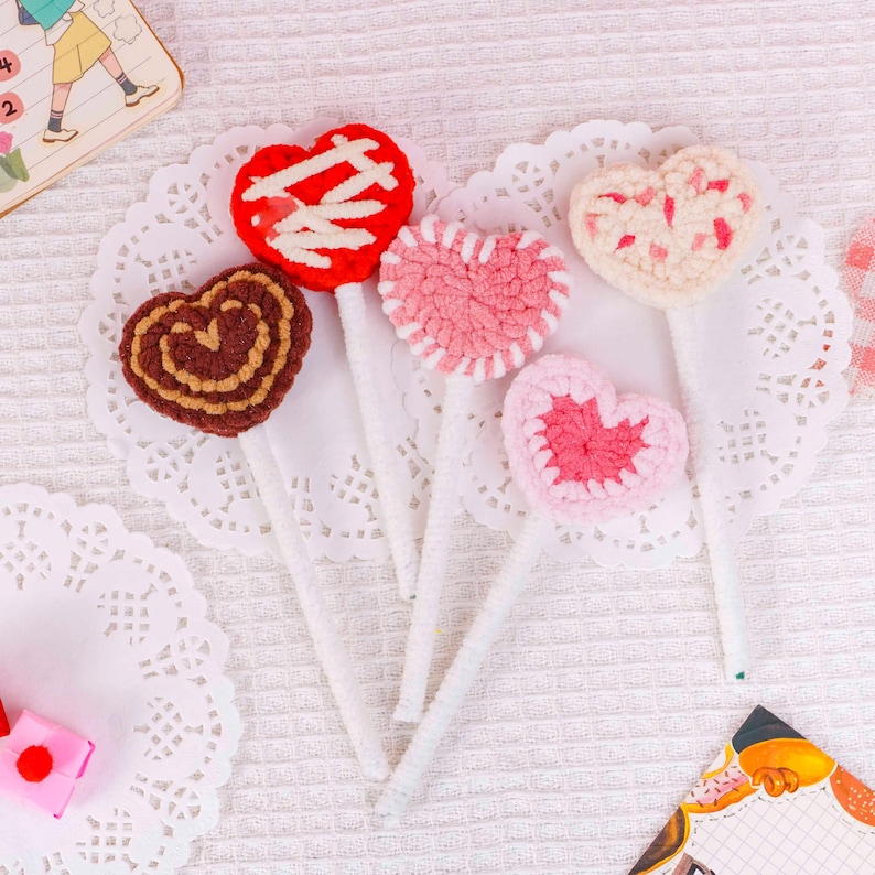 Puede incluir: Seis decoraciones hechas a mano en forma de coraz&oacute;n de ganchillo, en varios colores, incluyendo rojo, rosa y marr&oacute;n. Cada coraz&oacute;n est&aacute; unido a un palito blanco, similar a una piruleta. Los corazones est&aacute;n dispuestos sobre blondas blancas.