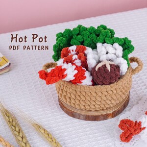 May include: A woven basket containing crocheted food items: green broccoli, red and white candy canes, and a brown mushroom. The basket rests on a wooden base. The text "Hot Pot PDF Pattern" is displayed.