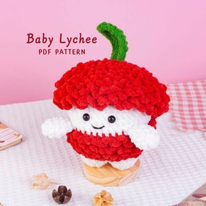 Può includere: Un giocattolo di peluche fatto a mano a forma di frutto di litchi, con un esterno rosso strutturato, una sezione centrale bianca e un gambo verde. Il giocattolo ha una faccia sorridente e braccia piccole. Il testo "Baby Lychee PDF Pattern" è visibile.