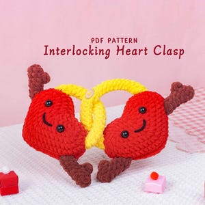May include: A handmade crochet heart clasp in red and yellow. The red hearts have smiling faces and brown stems. The clasp is connected by a yellow pretzel-shaped piece. Text on the image reads "PDF Pattern Interlocking Heart Clasp."