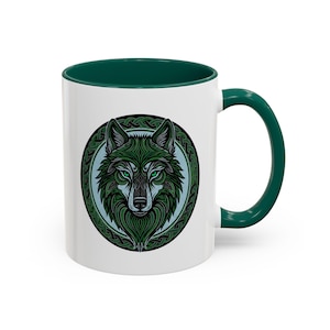 May include: White ceramic mug with a green interior and handle. The mug features a detailed green wolf design within a circular frame. The wolf has green eyes and intricate patterns, creating a striking contrast against the white background.