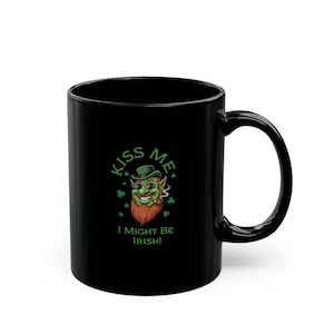 May include: Black ceramic mug featuring a green leprechaun graphic with a red beard, sunglasses, and a cigar. The mug has the text "Kiss Me, I Might Be Irish!" in green. A St. Patrick's Day themed mug.