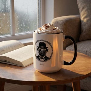 May include: A white ceramic mug with a black handle and rim, featuring a distinguished pug illustration in a black and white oval frame. The mug is filled with whipped cream and cocoa. The word "Pug" is printed below the illustration.