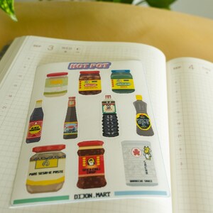 May include: A set of nine stickers featuring various Asian hot pot ingredients, including sesame paste, chili oil, and soy sauce. The stickers are arranged on a white background with the text "HOT POT" and "DIJON.MART" printed below.