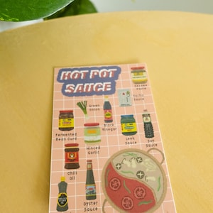 May include: A pink and white illustrated guide to hot pot sauce ingredients. The illustration shows a variety of sauces, spices, and vegetables, including fermented bean curd, black vinegar, leek sauce, soy sauce, green onion, minced garlic, chili oil, sesame oil, and oyster sauce. The illustration also includes a hot pot with a red and white yin yang design.