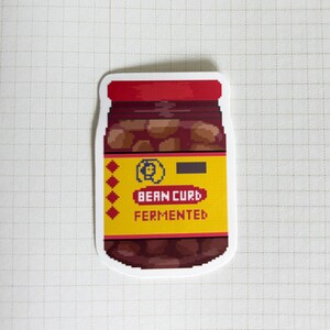 May include: A sticker of a jar of fermented bean curd. The jar is red and white with a yellow label that says "Bean Curd Fermented".
