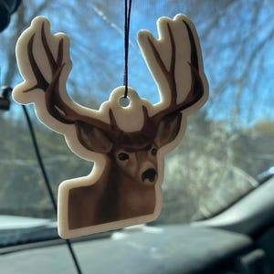 May include: A white car air freshener shaped like a deer with brown antlers and a brown face. The deer is looking to the right.