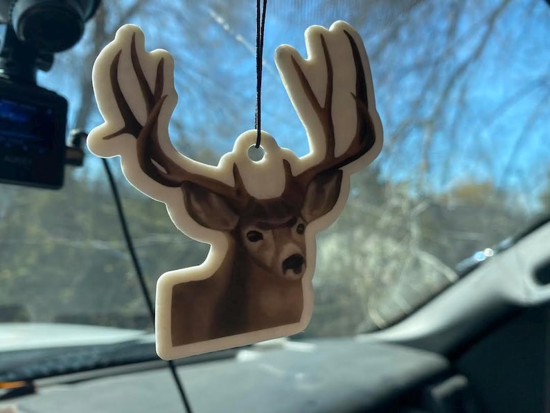 May include: A white car air freshener shaped like a deer with brown antlers and a brown face. The deer is looking to the right.