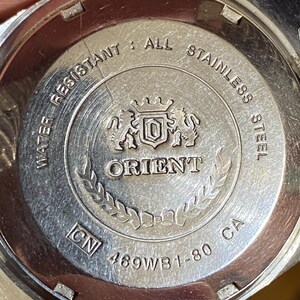 May include: Close-up of the back of a silver Orient watch. The watch back is engraved with the words "WATER RESISTANT", "ALL STAINLESS STEEL", and "ORIENT". The model number "469WB1-80 CA" is also visible.