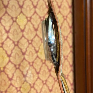 Może przedstawiać: Zegarek vintage z srebrną tarczą i brązowym sk&oacute;rzanym paskiem. Zegarek jest widoczny z boku, ukazując okrągłą tarczę i szczeg&oacute;ły szw&oacute;w paska. Pasek ma szerokość około 2 cm.