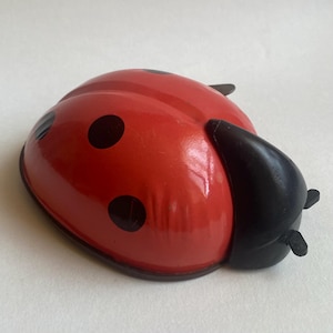 May include: A red ladybug toy with black spots and a black head. The ladybug is made of metal and has a shiny finish. The toy is a classic design, perfect for children.