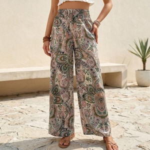 May include: Wide-leg paisley print pants in shades of green, pink, and beige. The pants have an elastic waistband and are worn with sandals. The paisley pattern is intricate and detailed, creating a bohemian aesthetic.